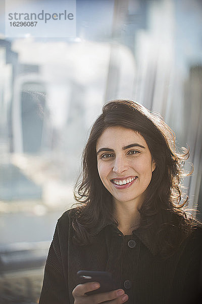 Porträt einer selbstbewusst lächelnden Geschäftsfrau mit Smartphone