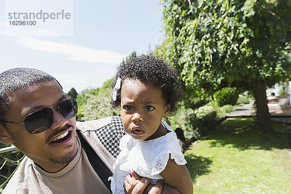 Vater hält neugierige Kleinkind-Tochter in sonnigen Sommerhinterhof