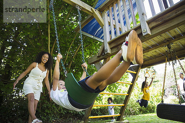 Fröhliche Familie beim Schaukeln und Spielen auf dem Spielplatz im Sommerhof