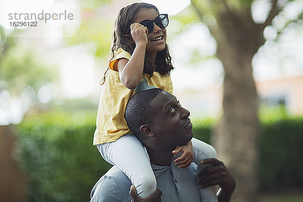 Vater trägt Tochter mit Sonnenbrille auf den Schultern