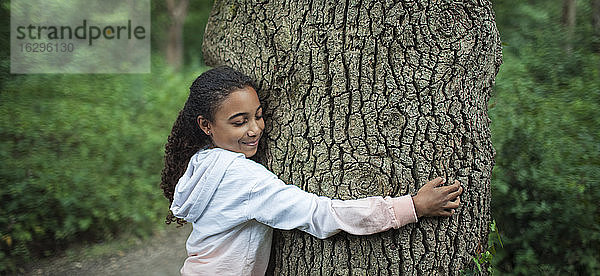 Gelassenes Mädchen umarmt Baumstamm im Wald