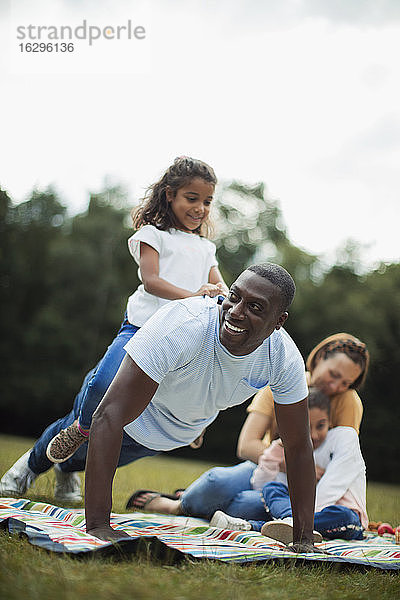 Verspielter Vater macht Push-ups mit der Tochter auf dem Rücken im Park
