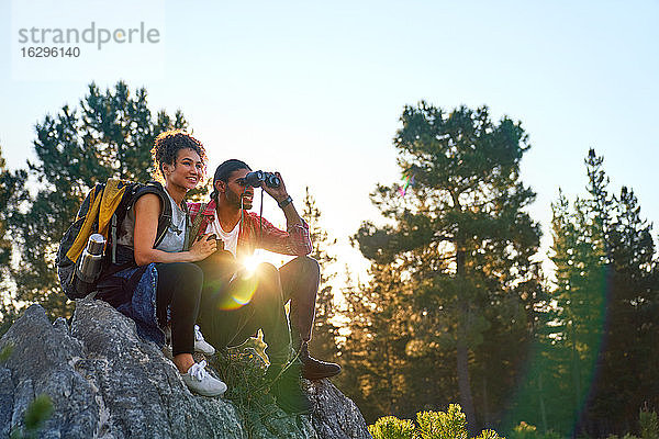 Junges Paar wandert mit dem Fernglas auf Felsen in sonnigen Wäldern