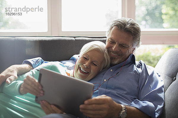 Glückliches älteres Ehepaar teilt Kopfhörer und digitales Tablett auf dem Sofa