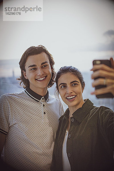 Glückliches junges Paar  das sich mit einem Fotohandy am Fenster selbstständig macht
