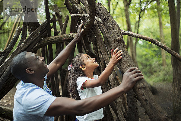 Vater und Tochter machen Tipi mit Zweigen im Wald