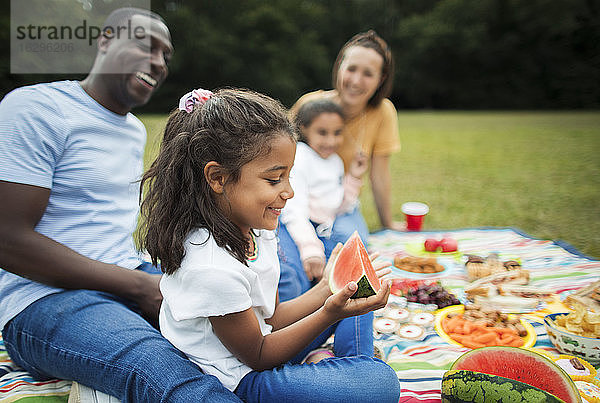 Glückliches Mädchen isst Wassermelone mit der Familie auf einer Picknickdecke im Park