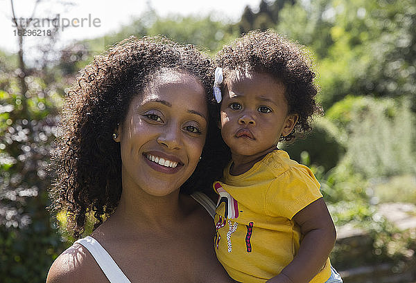 Porträt einer glücklichen Mutter und einer Kleinkind-Tochter in einem sonnigen Hof