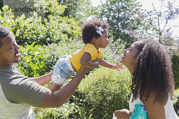 Liebevolle Eltern und Kleinkind-Tochter im sonnigen Sommergarten