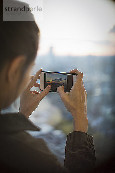 Frau mit Fotohandy fotografiert Sonnenaufgang über der Stadt