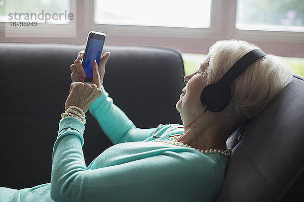 Ältere Frau entspannt sich mit Kopfhörern und Smartphone auf dem Sofa