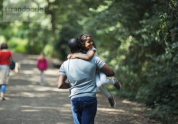 Verspielter Vater trägt glückliche Tochter auf Waldwegen