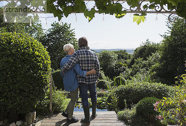 Liebenswertes älteres Ehepaar umarmt sich auf sonniger Sommergarten-Terrasse