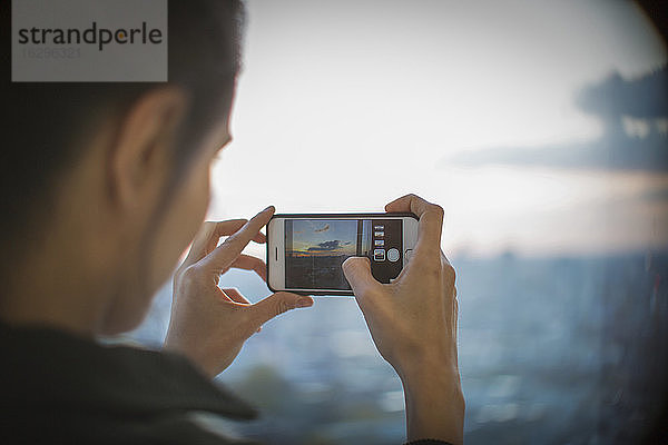 Frau mit Fotohandy fotografiert Sonnenuntergang am Hochhausfenster