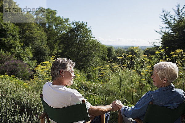 Liebenswertes älteres Ehepaar hält im sonnigen Sommergarten Händchen