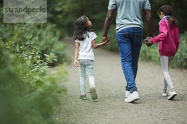 Vater und Töchter halten sich beim Spaziergang im Park an den Händen