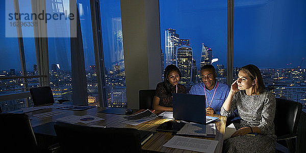 Geschäftsleute arbeiten spät am Laptop im Hochhaus-Konferenzraum
