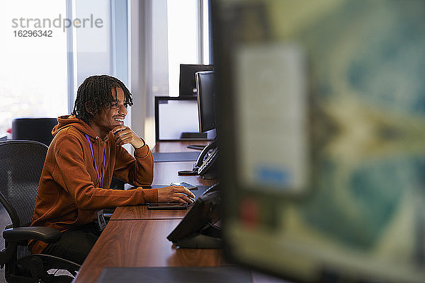 Lächelnder junger Geschäftsmann arbeitet am Computer im Büro