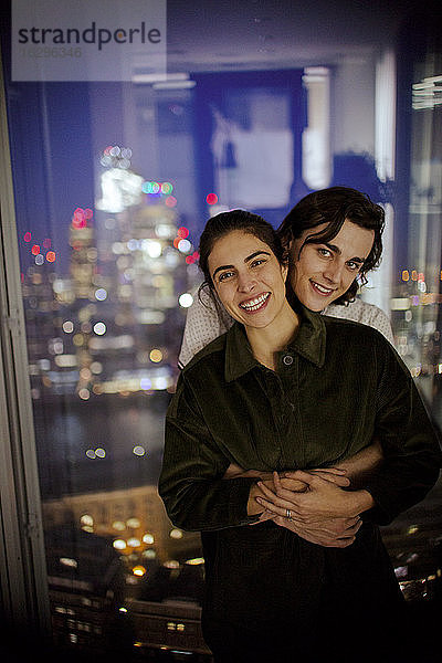 Porträt eines glücklichen jungen Paares  das sich am Hochhausfenster umarmt