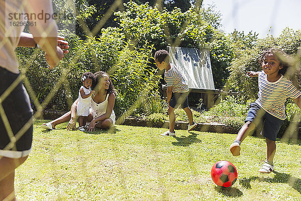 Glückliche Familie spielt Fussball im sonnigen Sommerhinterhof