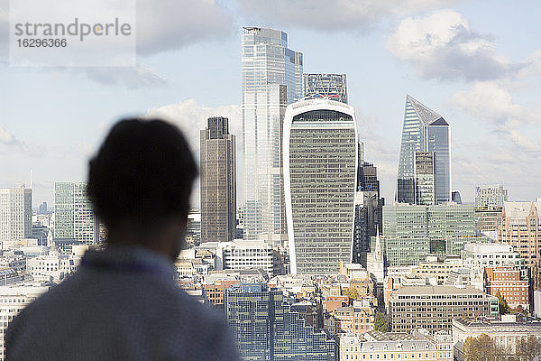 Geschäftsmann betrachtet die sonnige Londoner Stadtlandschaft vom Bürofenster aus  UK