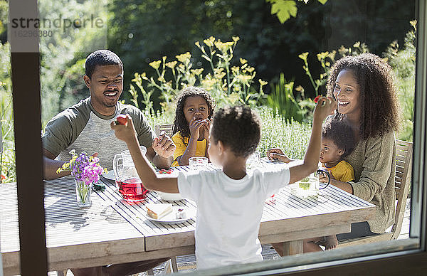 Glückliche Familie genießt das Mittagessen im Garten auf der sonnigen Sommerterrasse