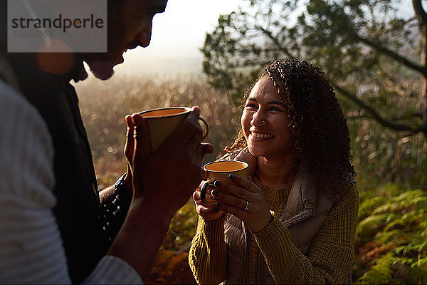 Glückliches junges Paar trinkt Kaffee in sonnigen Wäldern
