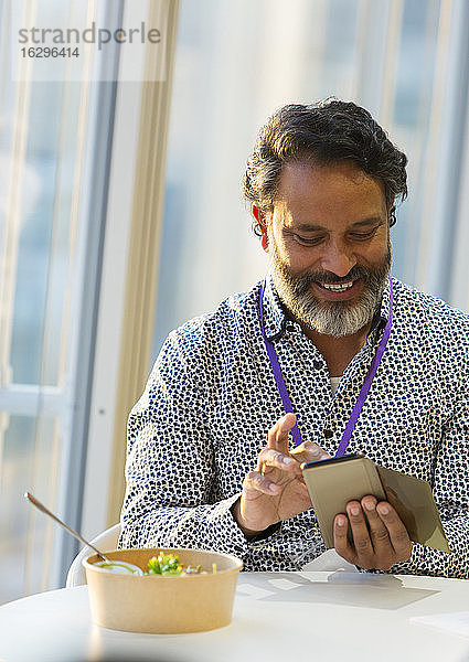 Lächelnder Geschäftsmann benutzt Smartphone beim Mittagessen