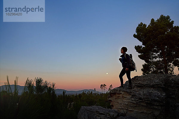 Junge Wanderin auf Fels in landschaftlich ruhiger Wüste in der Abenddämmerung