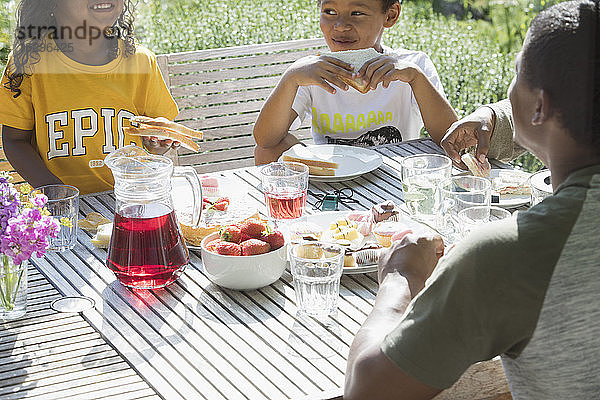 Familie beim Mittagessen an einem sonnigen Sommerterrassentisch