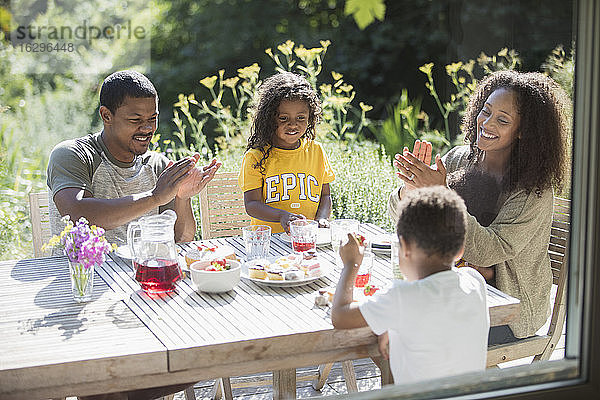 Glückliche Familie klatscht und isst am sonnigen Sommerterrassentisch