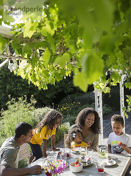 Glückliche Familie genießt das Mittagessen am sonnigen Sommergarten-Tisch