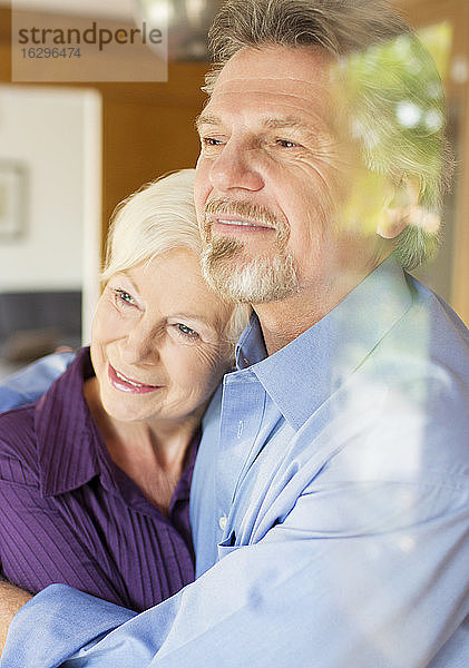 Gelassenes älteres Paar umarmt sich am Fenster