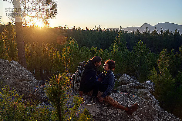Glückliches  liebevolles junges Paar entspannt sich bei Sonnenuntergang auf Felsen im Wald