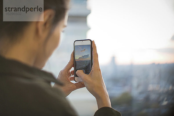 Frau mit Fotohandy fotografiert Sonnenuntergang vom Hochhaus