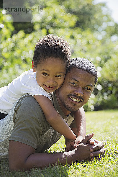 Porträt eines glücklichen Vaters und Sohnes  die sich im sonnigen Sommergras umarmen