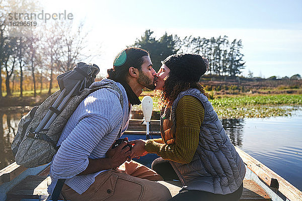 Zärtliches junges Paar küsst sich im Ruderboot auf einem sonnigen Herbstsee