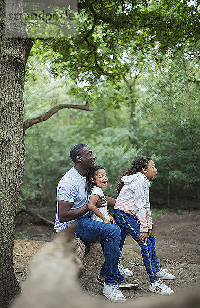 Glücklicher Vater und glückliche Töchter sitzen auf einem umgefallenen Baumstamm im Wald