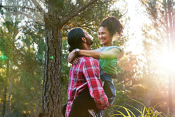 Zärtlicher junger Mann hält glückliche Freundin in sonnigen Wäldern