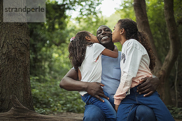Glückliche  liebevolle Töchter küssen Vater unter Bäumen im Wald