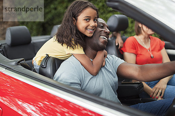 Porträt einer glücklichen Tochter  die ihren Vater umarmt  der ein Cabrio fährt