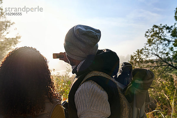 Junges Paar wandert und benutzt Fotohandy in sonnigen Wäldern