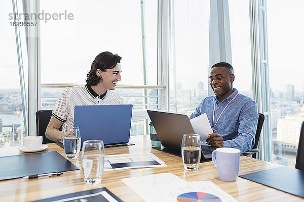 Lächelnde Geschäftsleute arbeiten an Laptops im Hochhaus-Konferenzraum