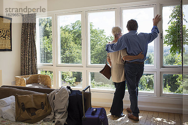 Liebevolles älteres Paar umarmt sich am sonnigen Mietfenster eines Hauses