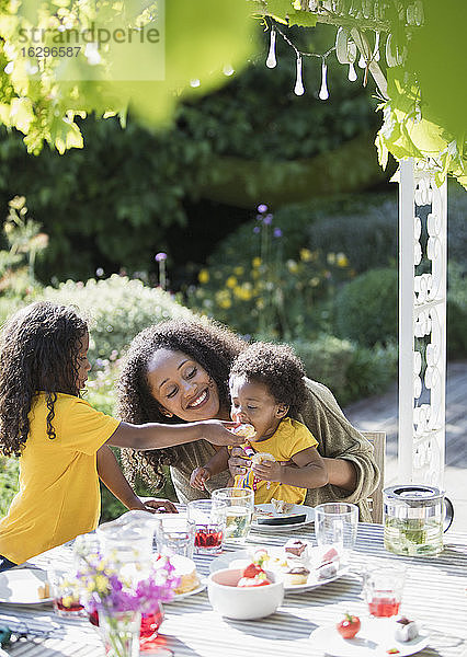 Glückliche Mutter und Töchter essen an einem sonnigen Sommer-Gartentisch