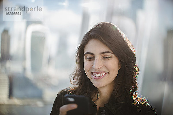 Lächelnde Geschäftsfrau benutzt Smartphone im sonnigen Fenster
