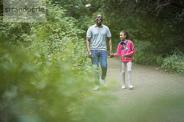 Glücklicher Vater und Tochter halten sich auf Waldwegen an den Händen