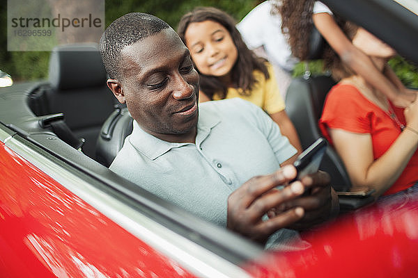 Mann benutzt Smartphone im Cabrio mit Familie