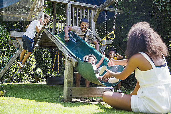 Familie spielt an einer Spielstruktur im sonnigen Sommerhinterhof