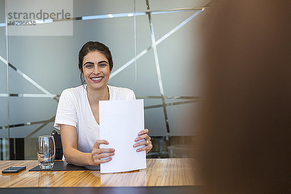 Porträt einer selbstbewusst lächelnden Geschäftsfrau mit Papierkram in einer Besprechung